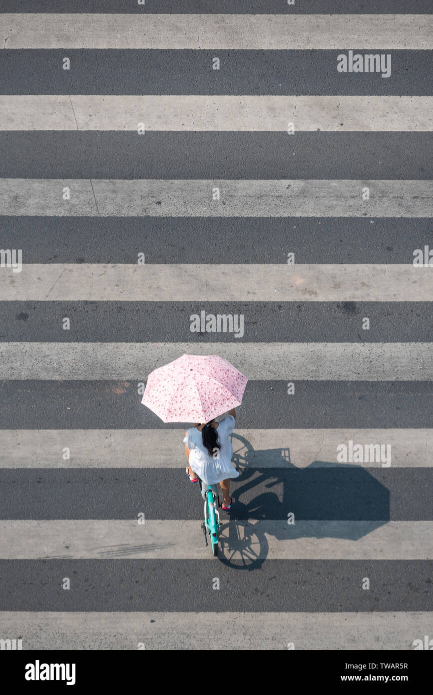 Chengdu, Provinz Sichuan, China - Juni 12, 2019: Junge chinesische Frau mit einem Regenschirm auf einem Zebrastreifen Antenne Top View an einem sonnigen Tag Stockfoto