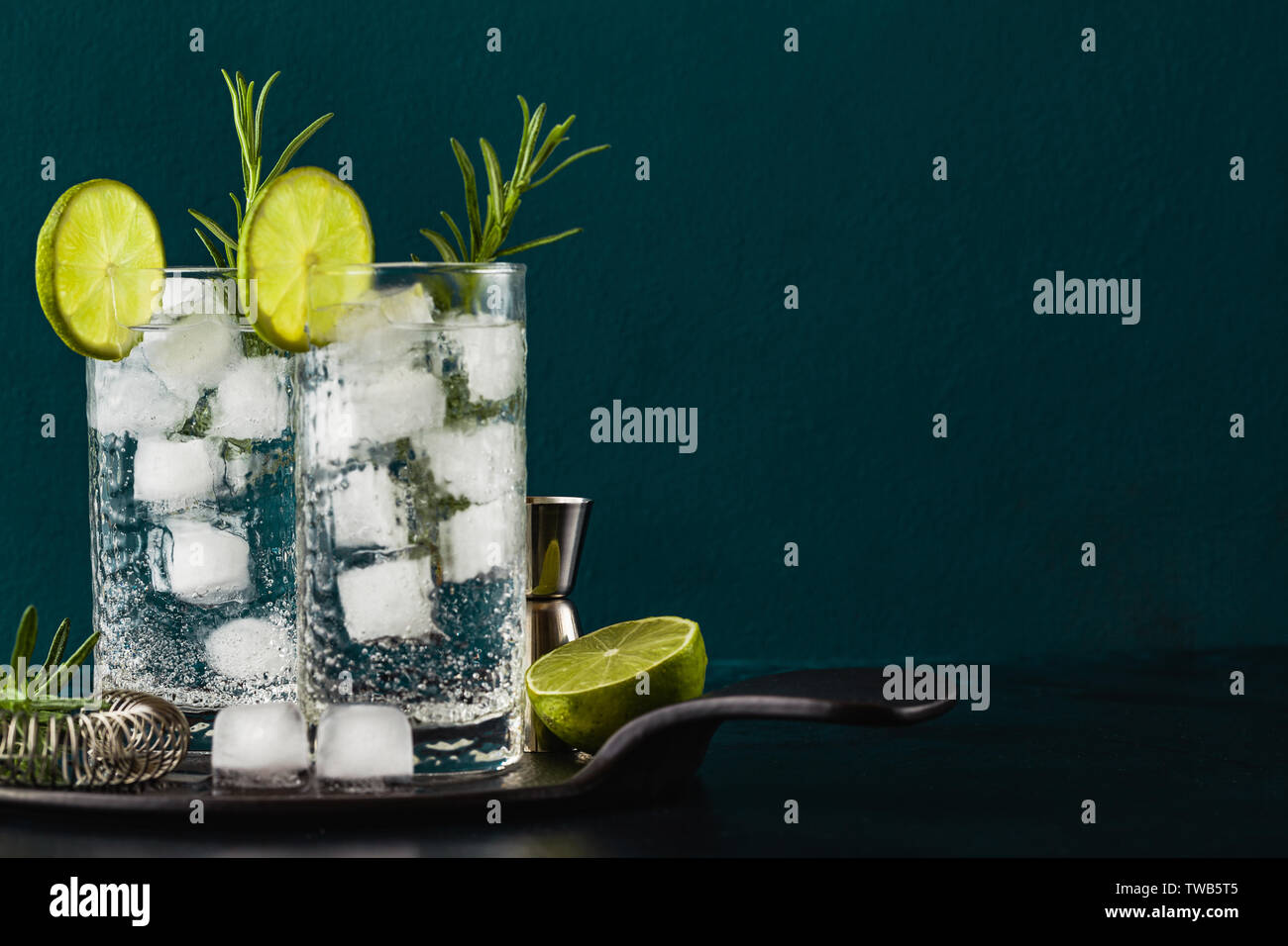 Classic Gin und Tonic Cocktail mit rosmarinzweige in hohe Gläser auf einem Tisch mit bar Zubehör Stockfoto
