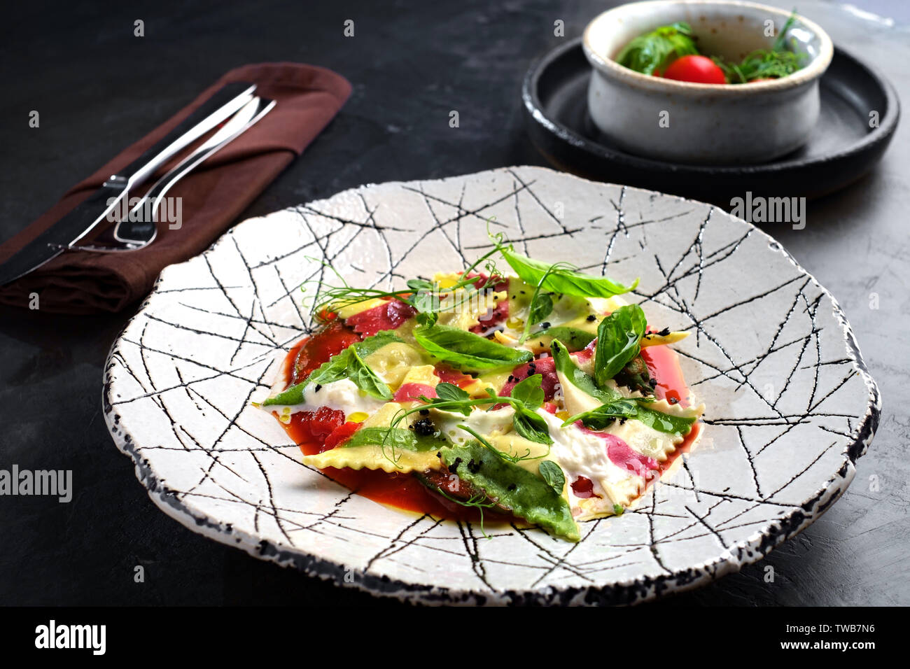 Сooked bunte Ravioli mit Spinat und Tomaten auf einer weißen Platte. Tisch aus Stein Stockfoto