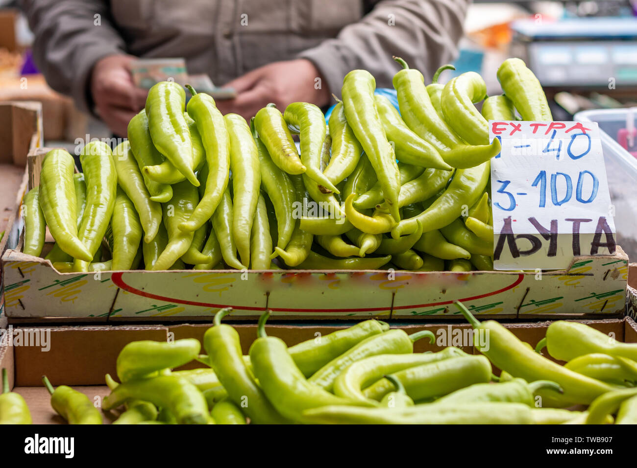 Stapel der grüne Pfeffer auf dem Stand bereit für den Verkauf auf dem Markt in Belgrad. Unscharfer Hintergrund des Verkäufers zählen Geld. Buchstaben "ЕXТPA ЉУТА' Me Stockfoto