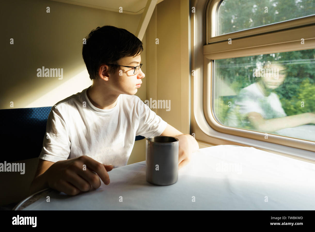 Ein Teenager boy in Gläsern auf einem Zug sitzt an einem Tisch mit Tee Stockfoto