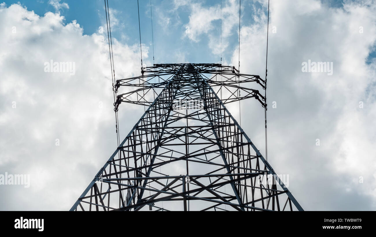 Ansicht von unten auf eine hohe Spannung Strom pylon gegen den blauen Himmel mit Wolken am sonnigen Tag. Hochspannungsnetzteil Sendeturm. Power Engineering. Stockfoto