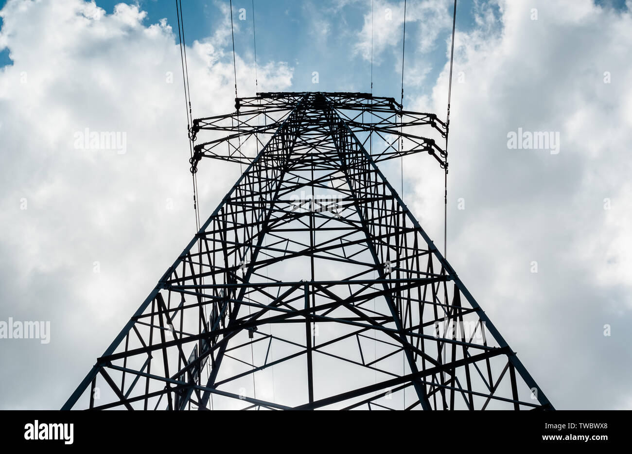 Ansicht von unten auf eine hohe Spannung Strom pylon gegen den blauen Himmel mit Wolken am sonnigen Tag. Hochspannungsnetzteil Sendeturm. Power Engineering. Stockfoto