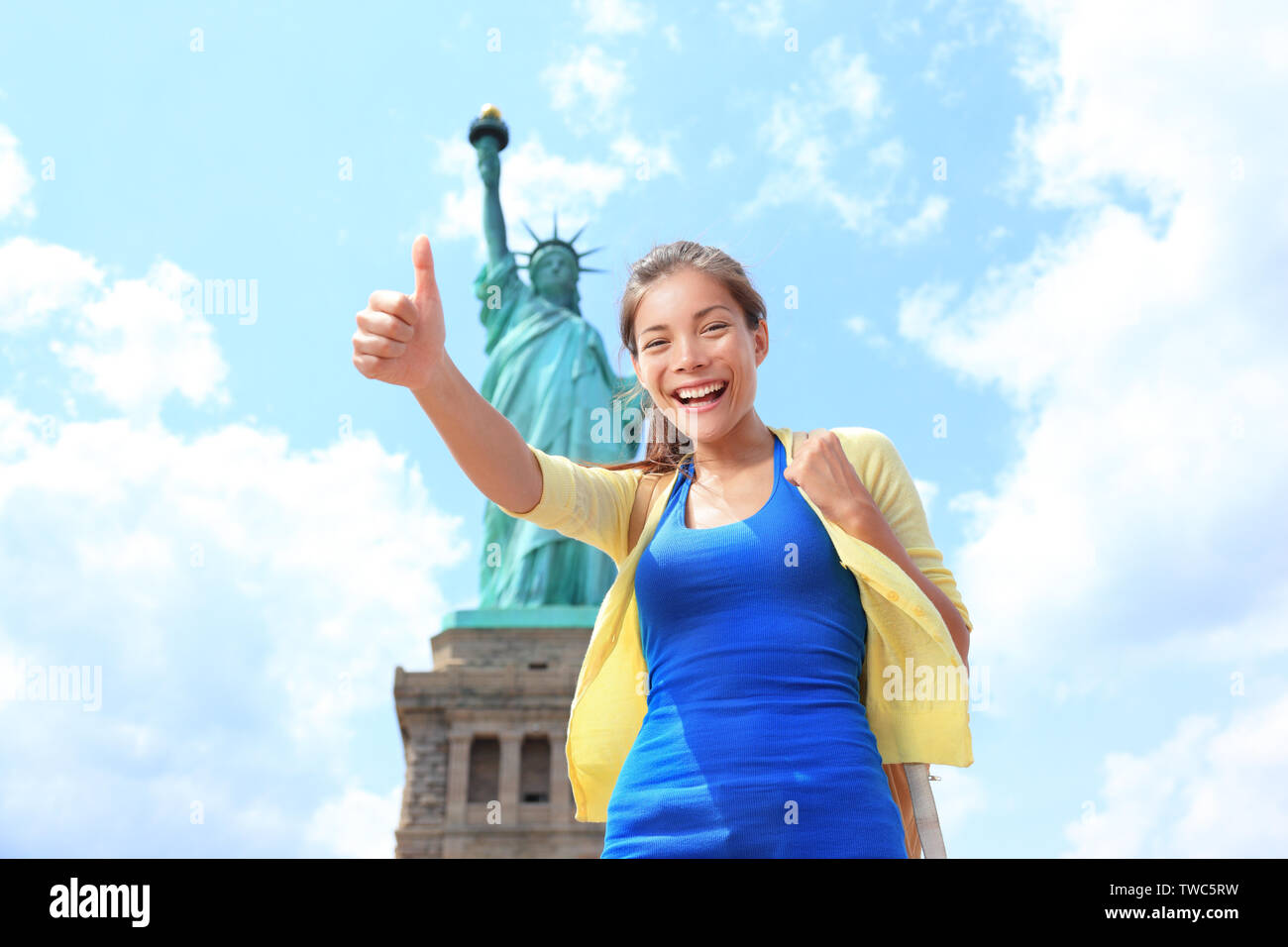 New York City die Freiheitsstatue touristische Frau geben Daumen nach oben. Happy girl auf Tourismus Reisen auf Liberty Island, USA. Jungen multiethnischen alleinreisende Frau Spaß zu haben. Asiatische kaukasische Frau. Stockfoto