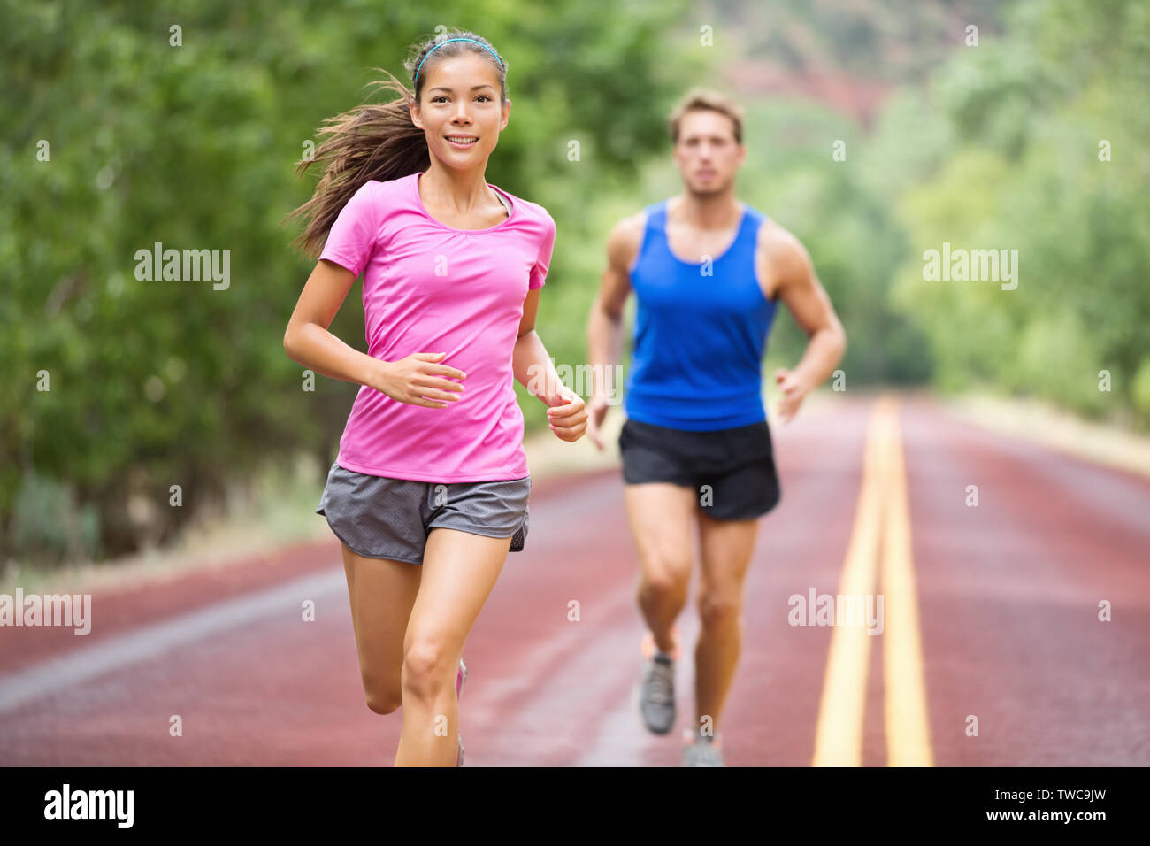 Ausführen von jungen gemischten Rennen paar Training für Marathon draußen auf der Straße. Glücklich lächelnde schönen gemischten Rennen weibliche model in der Stattlichen kaukasischen männliches Modell im Hintergrund verschwommen, auf denen fokussierte Stockfoto