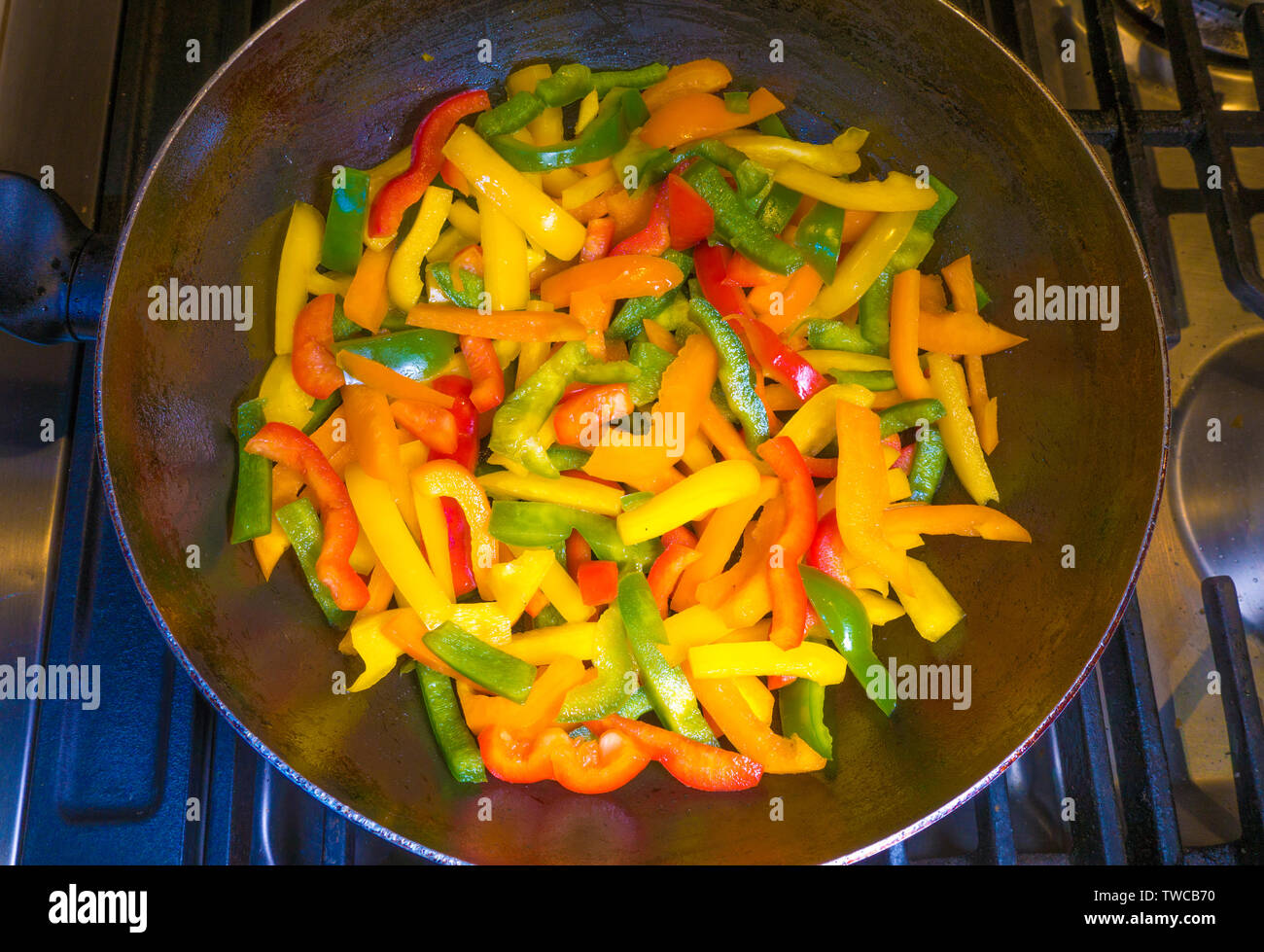 Ein Wok mit Paprika verschiedener Farben, über gebraten auf einem Kochfeld. Stockfoto