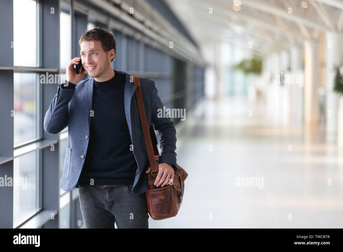 Urban Business Mann auf smart phone Reisen im Walking im Flughafen. Lässige junge Unternehmer tragen Anzug Jacke und Umhängetasche. Stattliche männliche Modell in seiner 20. Stockfoto