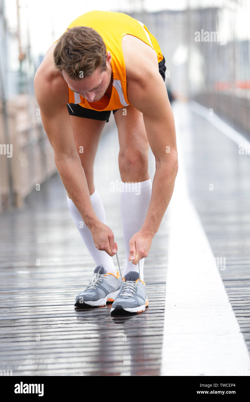 Zweiter Mann binden Schnürung an Laufschuhe, New York City auf der Brooklyn Bridge. Männliche Athlet runner und Füße Nahaufnahme. Fitness model Kompressionsstrümpfe tragen. Stockfoto
