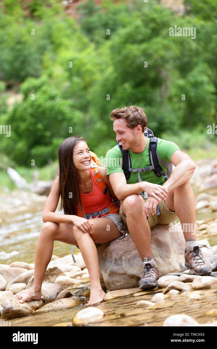 Wandern Menschen - Wanderer Paar im Zion National Park gerne reden und Ausruhen. Junge Frau und Mann Wanderer sitzen durch Wasser des Flusses Creek genießen Aussicht lächelnd. Junges Paar entspannend nach der Wanderung, Utah, USA. Stockfoto