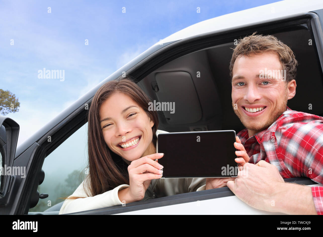 Tablet PC - Paar fahren im Auto mit Bildschirm mit App oder Nachricht. Junge glücklich Treiber auf Road Trip. Asiatische Frau, kaukasische Mann. Stockfoto
