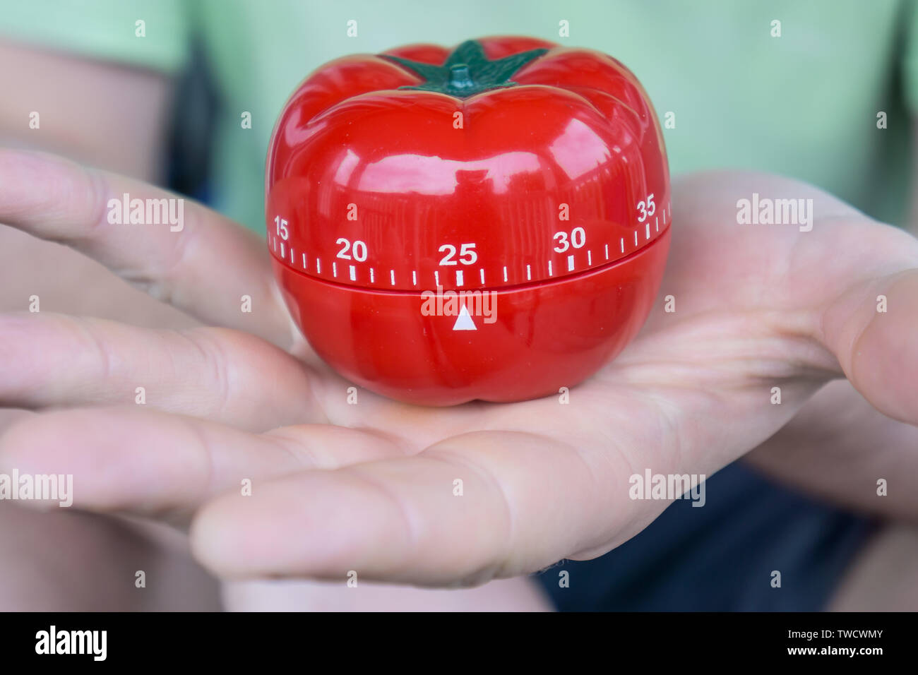 Mechanische rote Tomate Küche Timer bis 25 Minuten einstellen, durch eine Person mit einer offenen Hand hielt. Alte Schule Produktivitätstool für Zeitmanagement und Procr Stockfoto