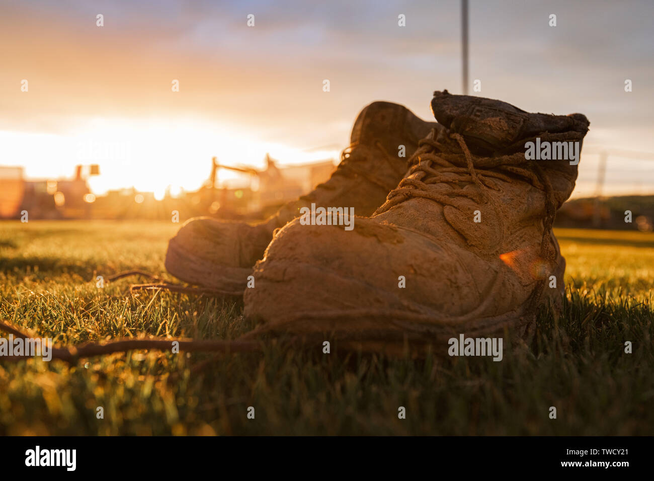 Sicherheitsstiefel auf einer Baustelle im Schlamm, die vor einem hellen Sonnenuntergang abgedeckt Stockfoto