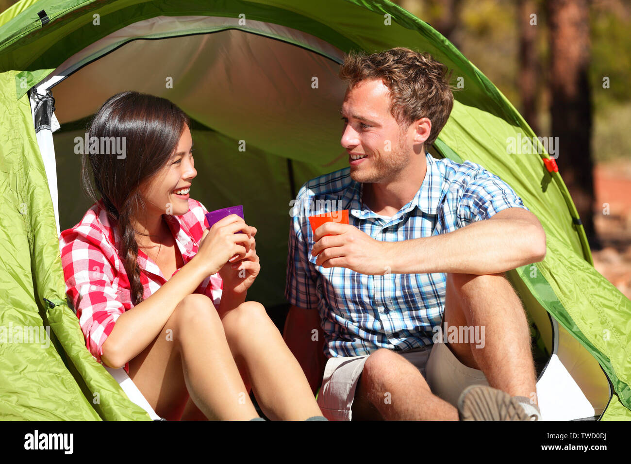 Camping paar Trinkwasser in Zelt Lächeln glücklich draußen in Wald Sonne genießen am Betrachten der Ansicht. Happy gemischtrassiges Paar entspannend nach Aktivität im Freien wandern. Asiatische Frau, kaukasische Mann. Stockfoto