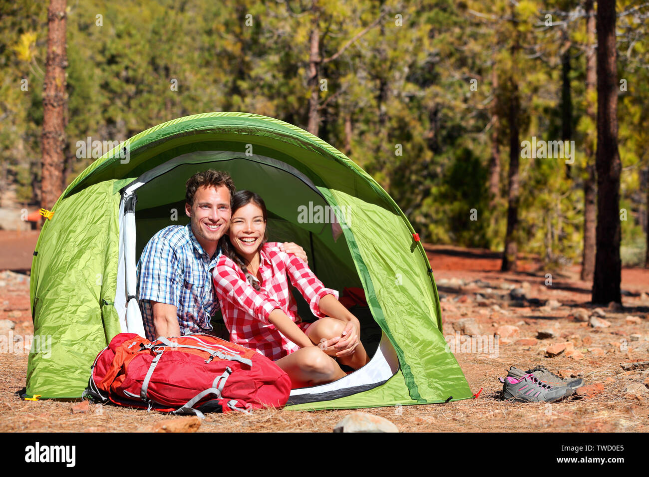 Auf dem Campingplatz im Zelt - glückliche backpacking Paar im Wald. Camper lächelt glücklich draußen im Wald. Happy gemischtrassiges Paar Spaß entspannen in Aktivitäten im Freien. Asiatische Frau, kaukasische Mann Stockfoto