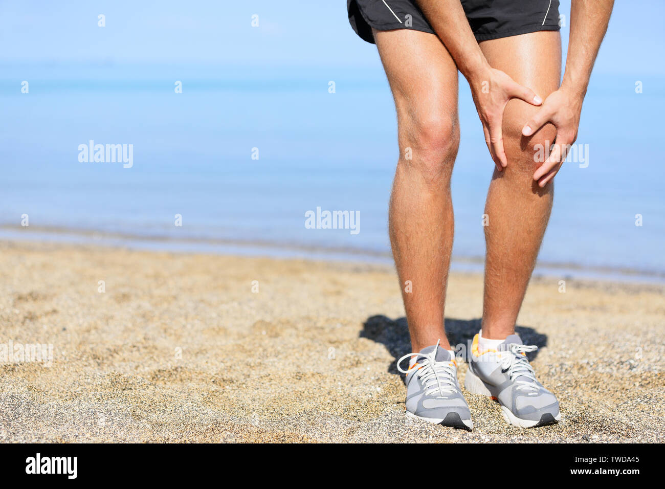 Ausführen von Verletzungen - Mann joggen mit Knieschmerzen. Nahaufnahme der Runner verletzt Jogging am Strand seine Knie zu schmerzen. Männliche fitness Sportler. Stockfoto