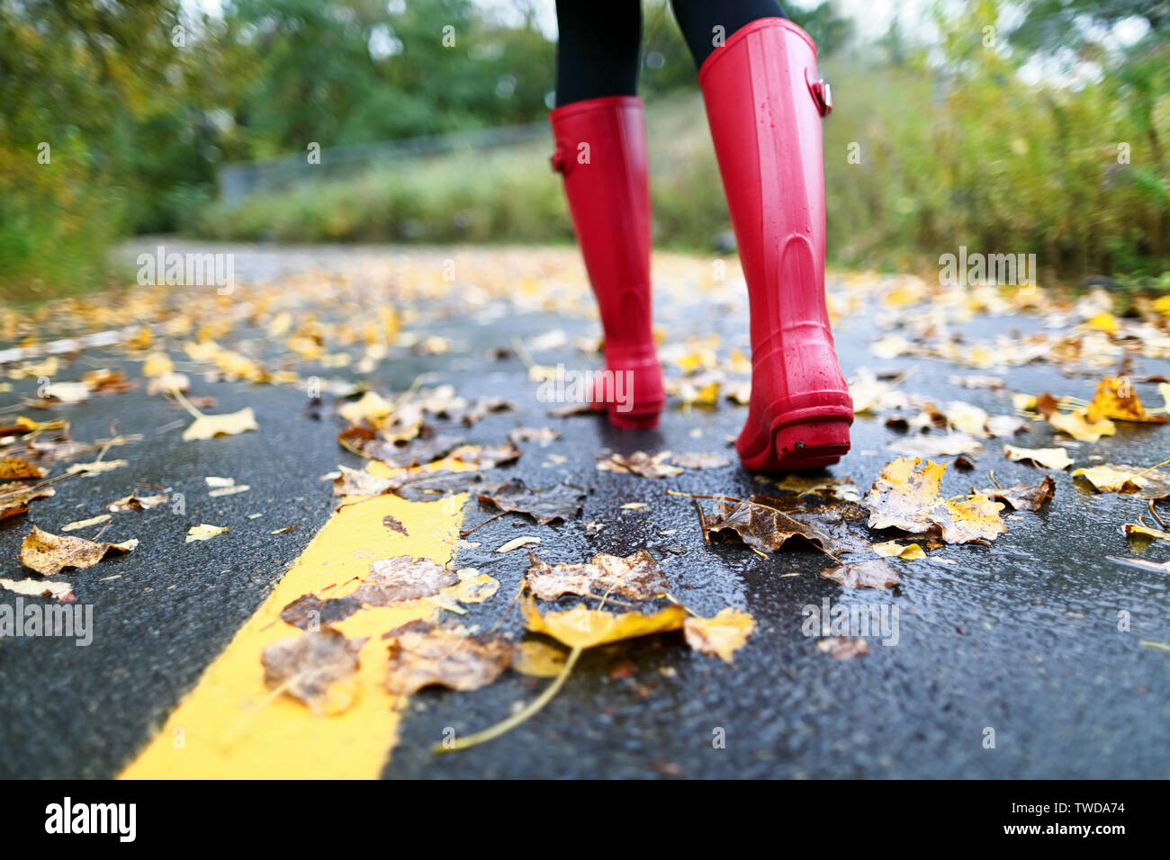 Herbst Herbst Konzept mit bunten Blättern und regen Stiefel außerhalb. Nahaufnahme von Frau Fuß zu Fuß in roten Stiefel. Stockfoto