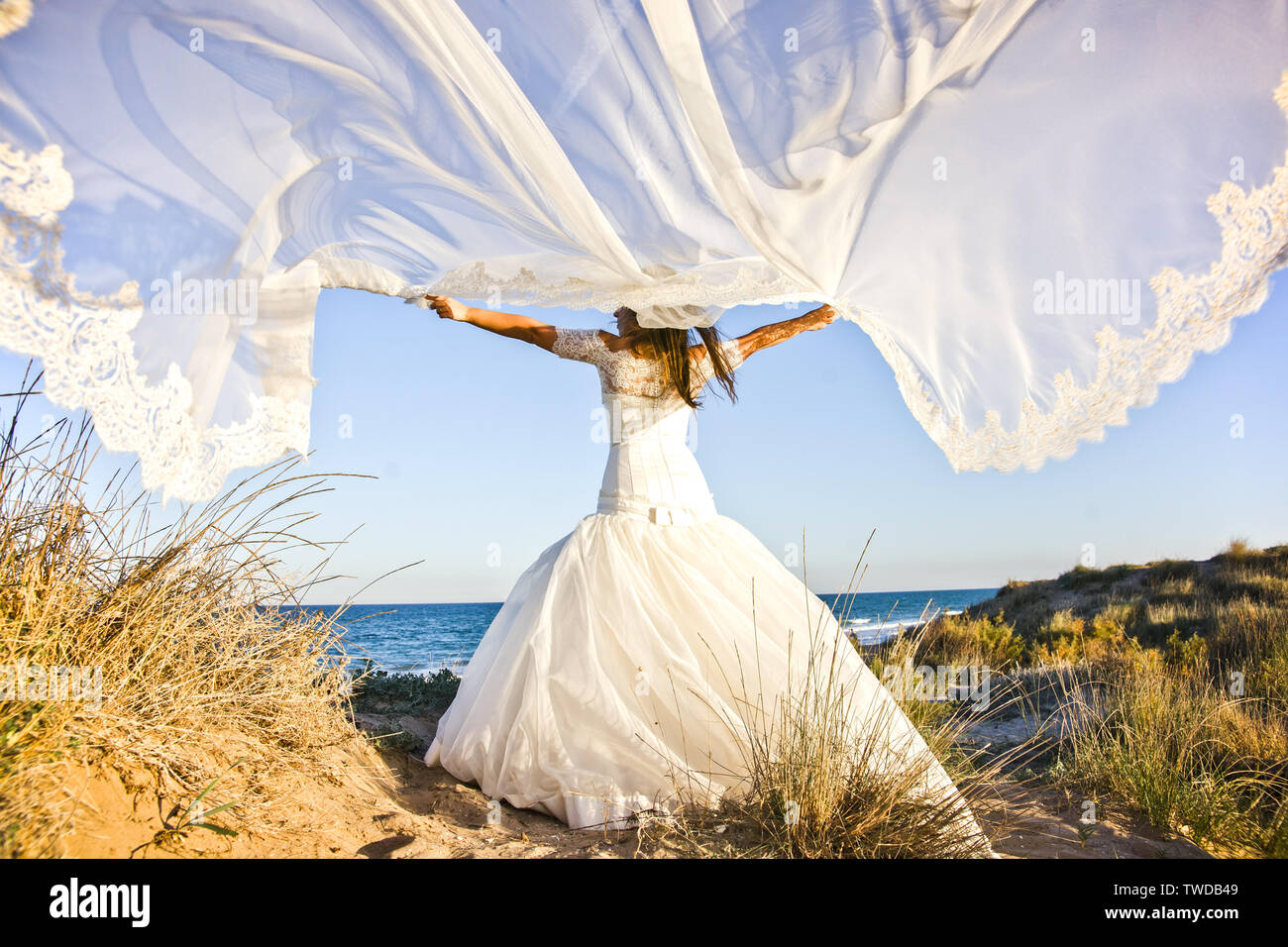 Glückliche Braut mit ihrem Hochzeit Kleid weht, ihren Schleier zu der Wind  am Strand Stockfotografie - Alamy