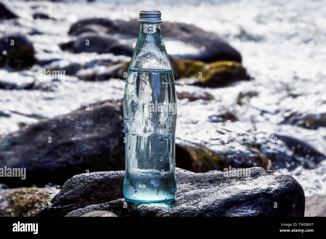 Eine Flasche frisches, kühles Wasser vor dem Hintergrund der Natur, einem Gebirgsfluss mit reinstem Wasser. Stockfoto