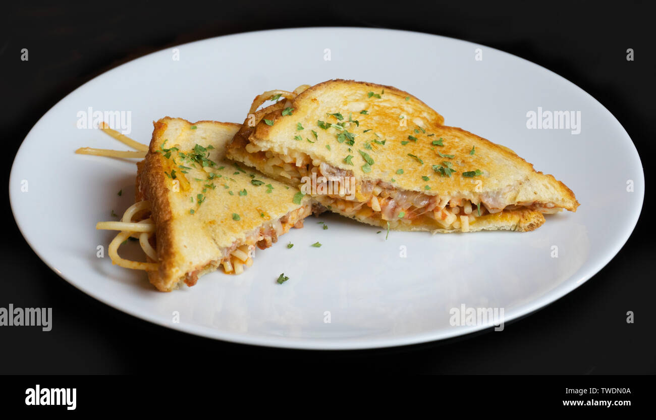 Ein Spaghetti gegrillter Käse Sandwich Mash Up. Hausgemachte Fusion auf eine weiße Platte mit einem schwarzen Hintergrund. Die Kombination von zwei Heften homestyle Comfort Foods. Stockfoto