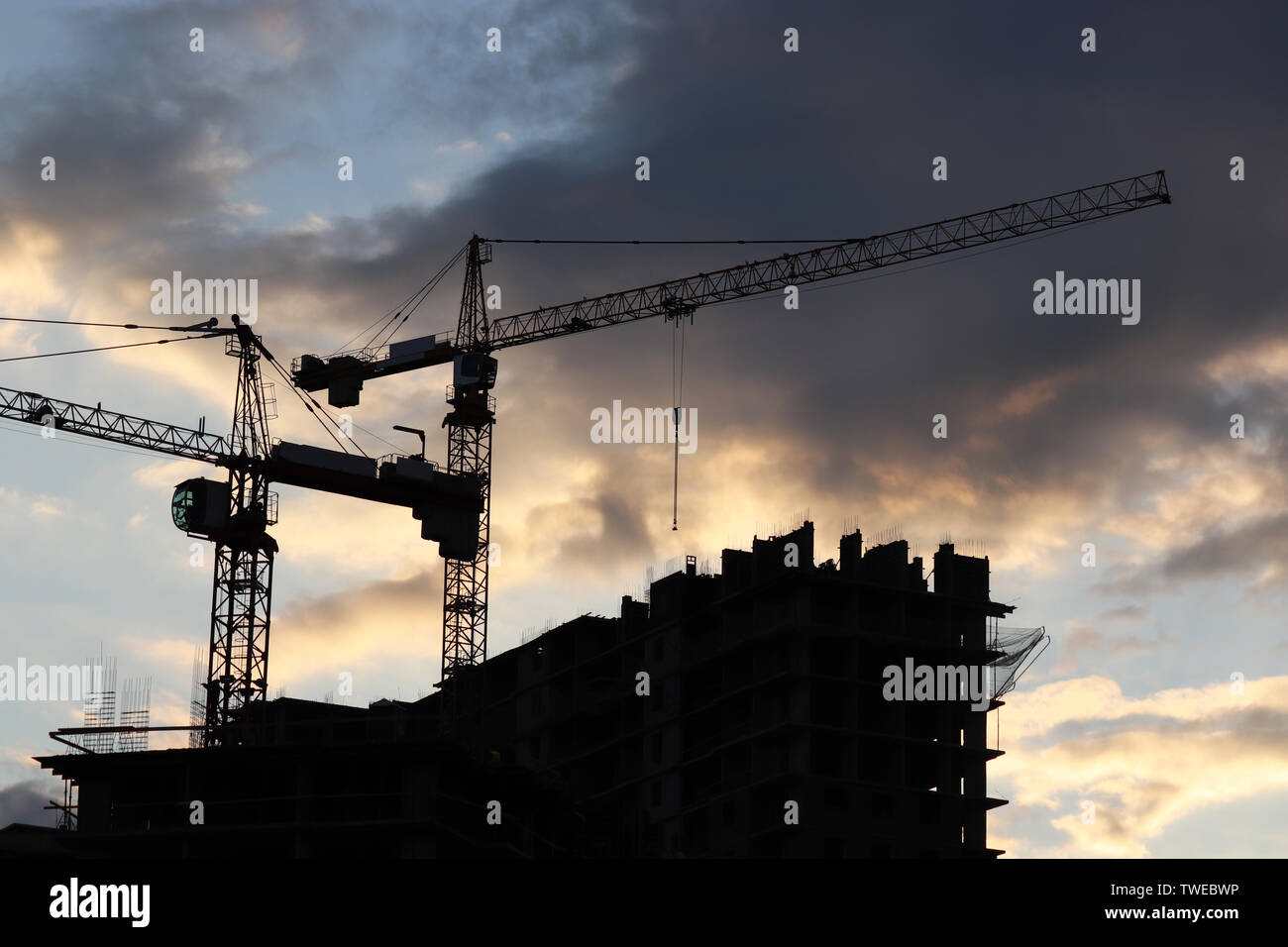 Silhouetten der beiden baukräne und Wohngebäude gegen den Abendhimmel mit Wolken. Baustelle am Sunset Stockfoto