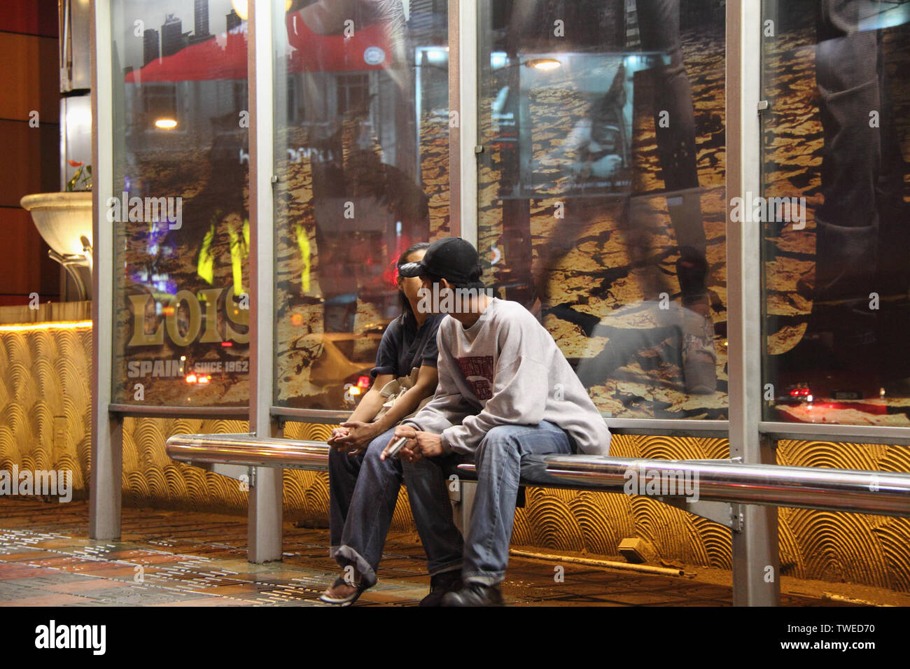 Ein Paar sitzt an einer Bushaltestelle, Kuala Lumpur, Malaysia Stockfoto