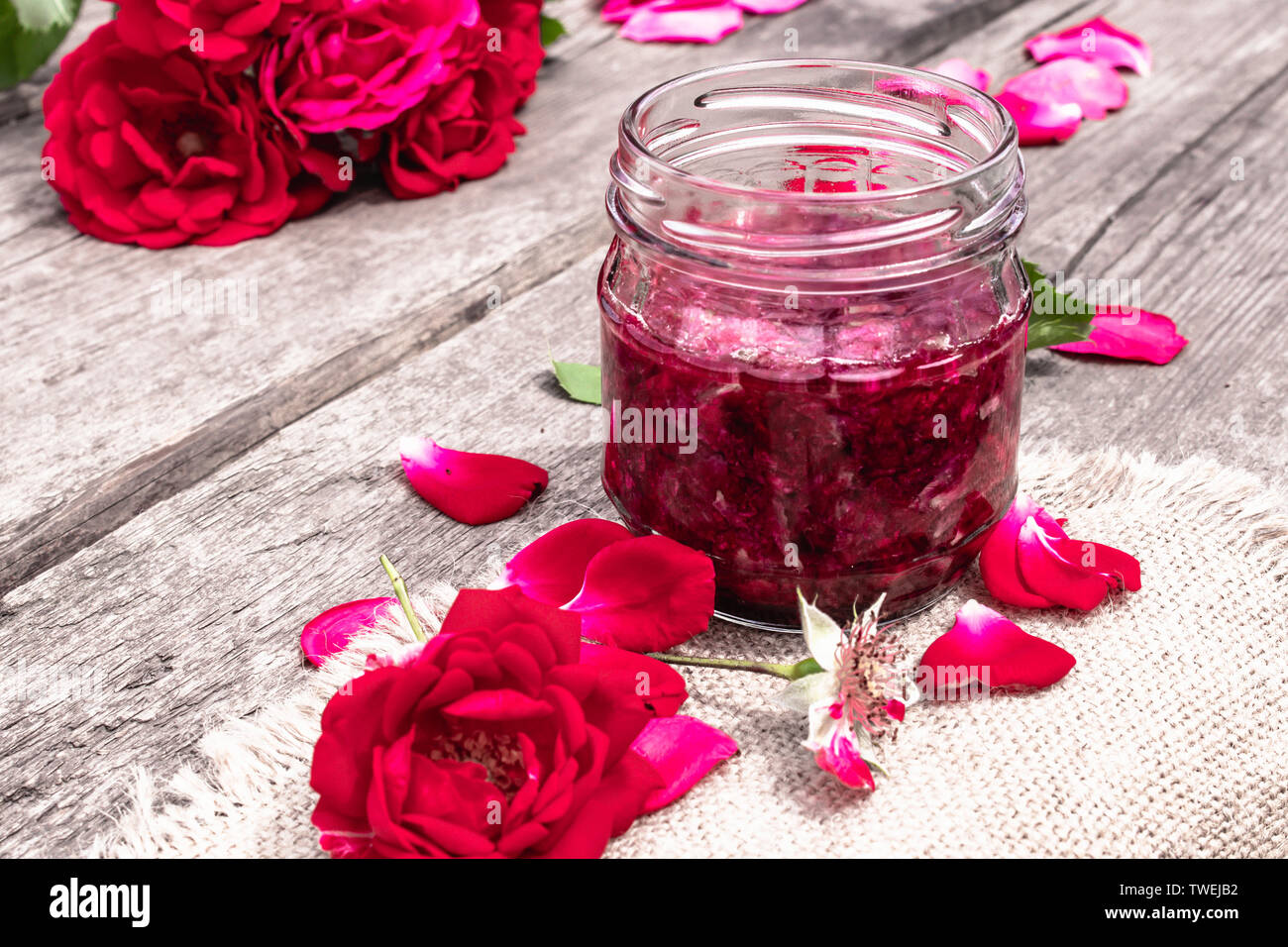 Marmeladenglas von Rosenblättern auf einen hölzernen Tisch mit Blüten von Rosen. Blume Konfitüre. Gesundes Essen. Platz kopieren Stockfoto
