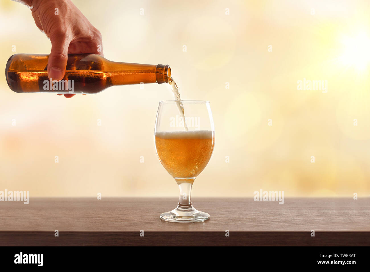Hand Bier Flasche füllen Sie ein Glas Schale auf Holztisch und goldenem Hintergrund. Horizontale Komposition. Vorderansicht. Stockfoto
