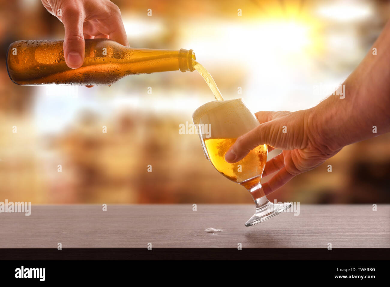 Hände füllen ein Bier Glas aus einer Glasflasche auf einer hölzernen Bar in der Freizeit statt. Horizontale Komposition. Vorderansicht. Stockfoto