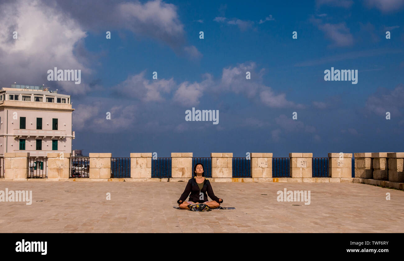 Frau sitzt auf ihrem eigenen im Lotussitz meditierend in Ortygia in Syrakus auf Sizilien. Stockfoto
