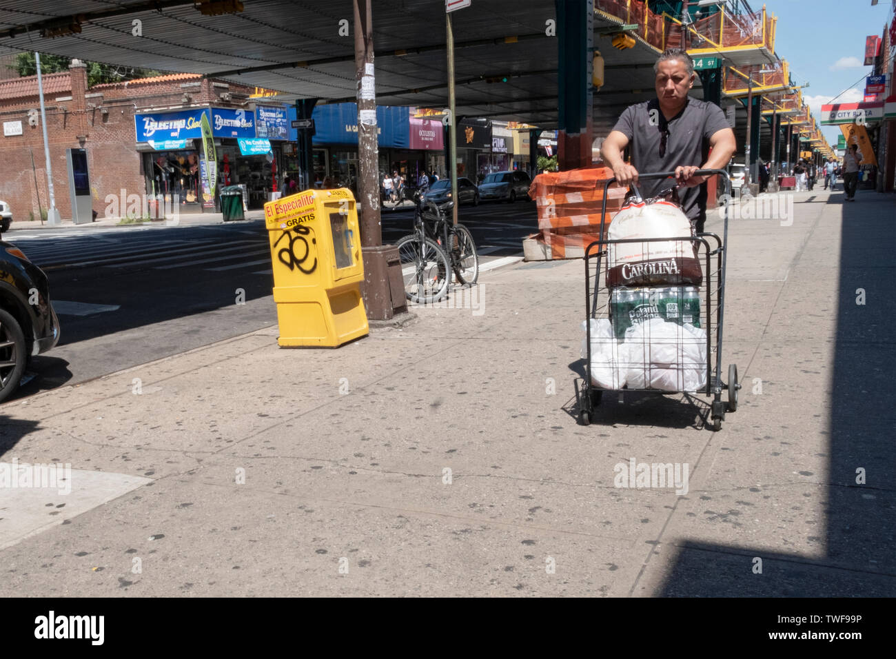 Ein Mann, der wahrscheinlich in Lateinamerika, schiebt einen Einkaufswagen mit Lebensmitteln und Wasser unter der El an der Roosevelt Ave & 84th St. in Jackson Heights, Queens, NYC Stockfoto