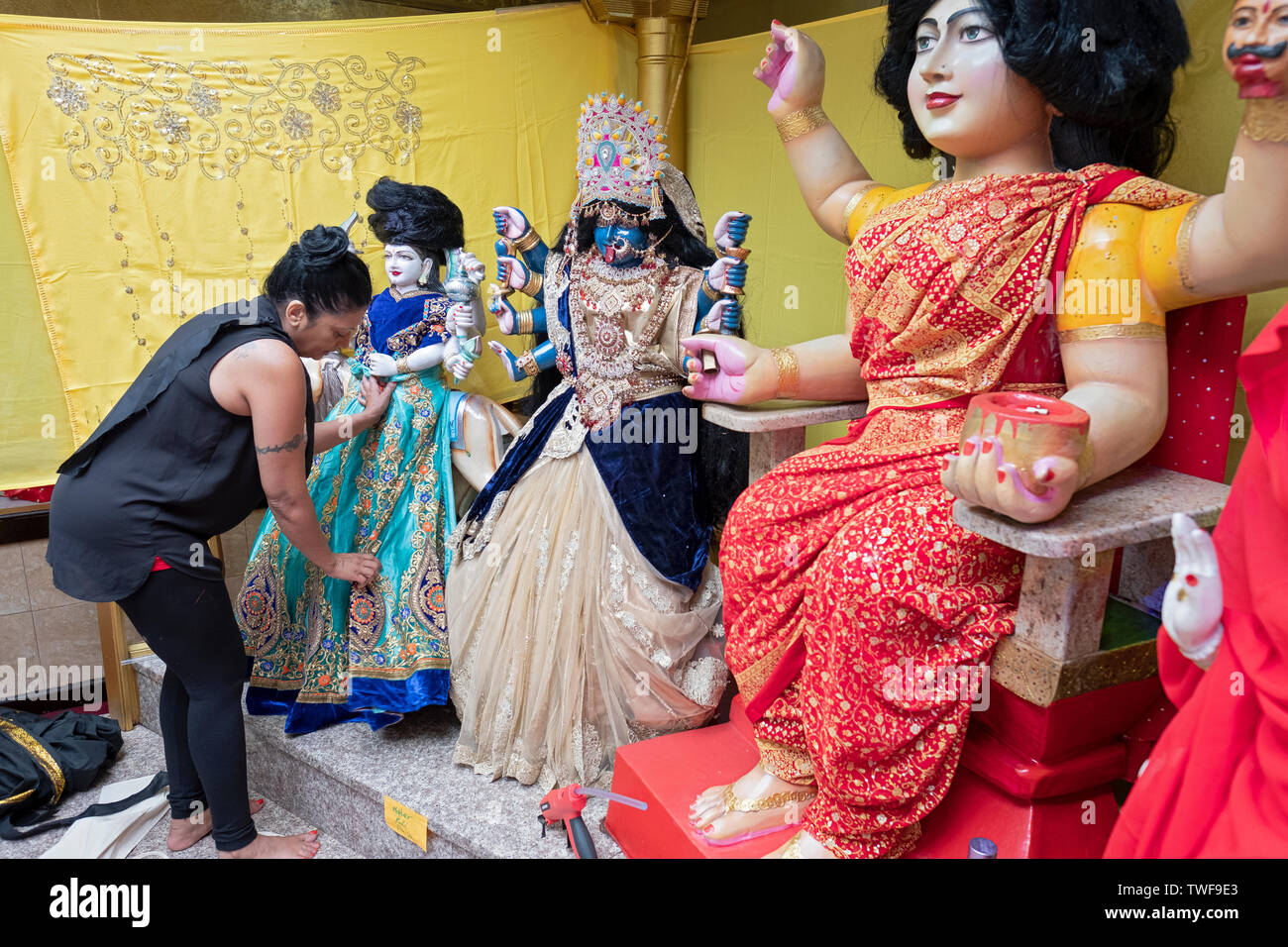 Als Teil einer Danksagung Ritual, eine fromme Frau entworfen und installiert neue Kleidung auf dem Tempel Statuen von Gottheiten. In Ozone Park, Queens, NYC Stockfoto