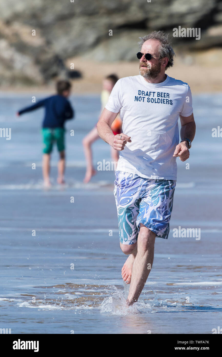 Ein reifer Mann, der ein T-Shirt mit einem lustigen Slogan Joggen entlang der Küste auf den Fistral Beach in Newquay in Cornwall. Stockfoto