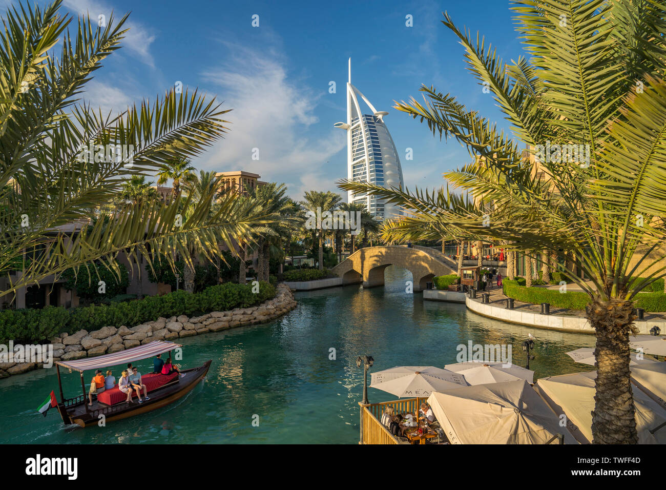 Ein abra Boot gleitet durch das blaue Wasser des Souk Madinat Jumeirah als Segel - wie das Burj al Arab steigt Overhead. Stockfoto