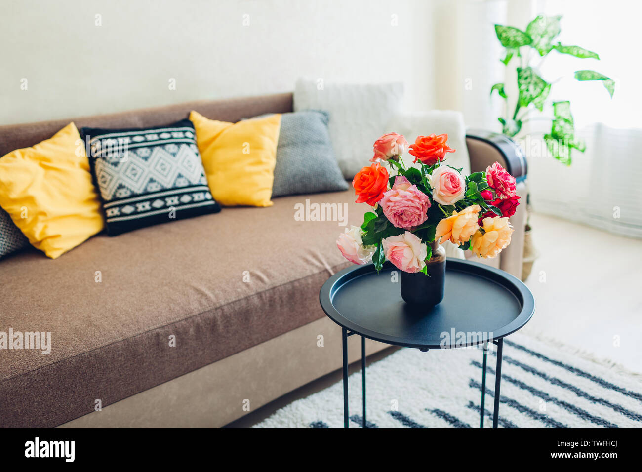 Innenraum der Wohnzimmer mit Blumen am Kaffeetisch und gemütliches Sofa mit Kissen dekoriert. Blumenstrauß aus farbenfrohen frische Rosen Stockfoto