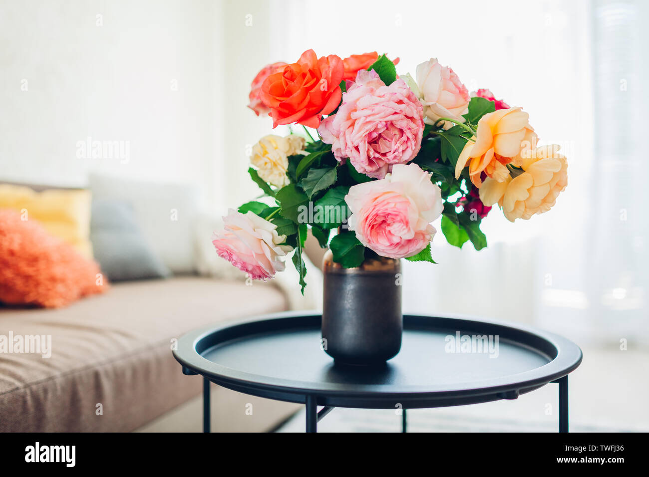 Innenraum der Wohnzimmer mit Blumen am Kaffeetisch und gemütliches Sofa mit Kissen dekoriert. Blumenstrauß aus farbenfrohen frische Rosen Stockfoto
