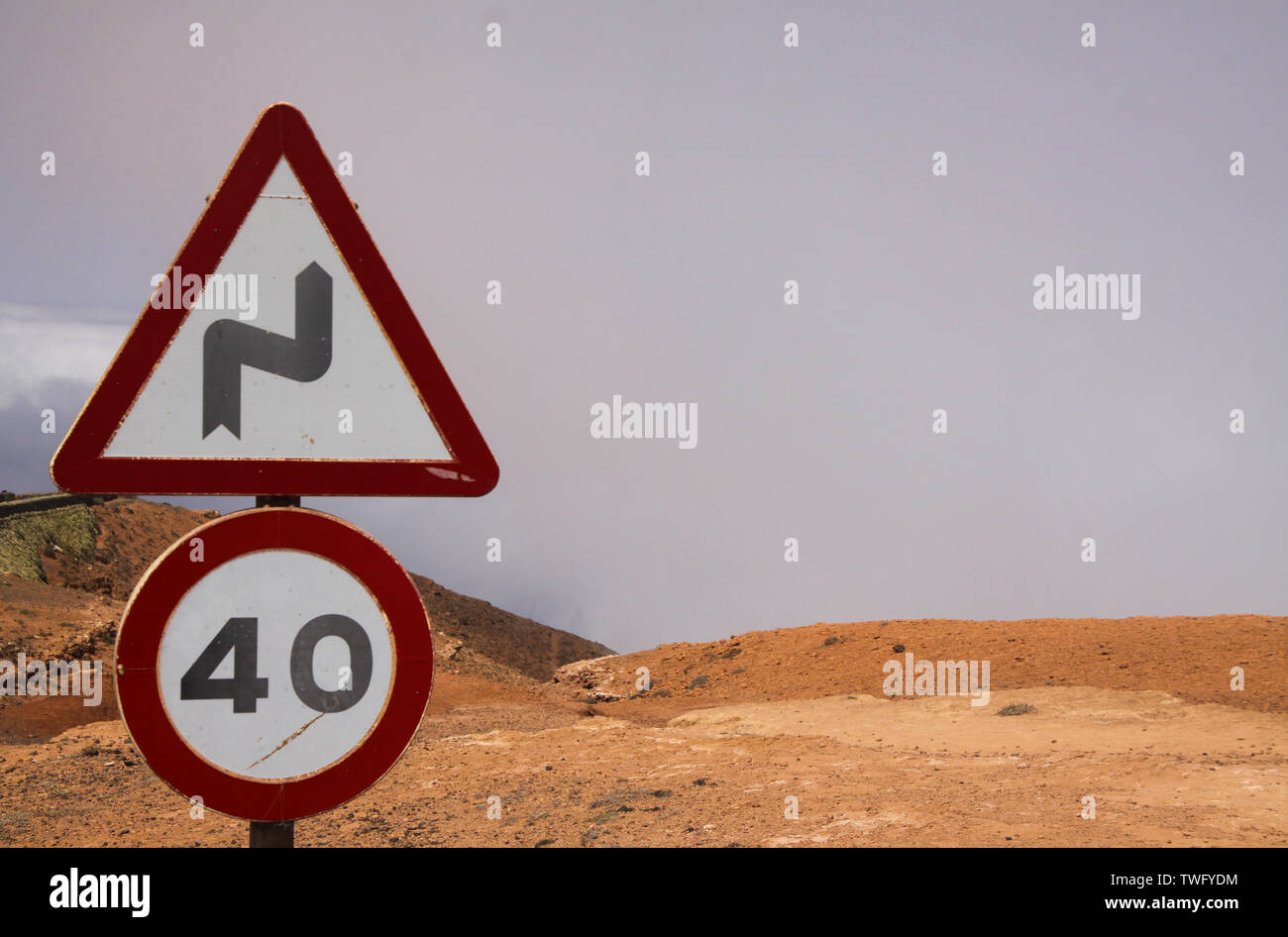 Mirador del Rio - Lanzarote: Nahaufnahme von Tempo 40 Schild und Warnung für Kurven Zeichen über den Wolken auf dem Trockenen Berg (Fokus auf der linken Seite Schild) Stockfoto