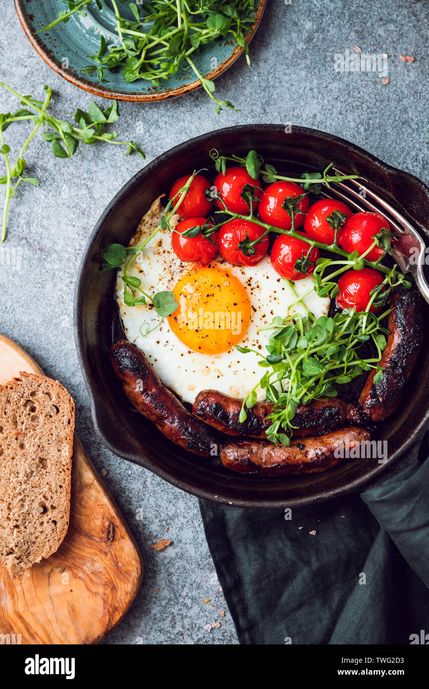 Frühstück, Rührei mit Würstchen und Cherry Tomaten in einem schwarzen eiserne Pfanne, microgreens serviert. Stockfoto