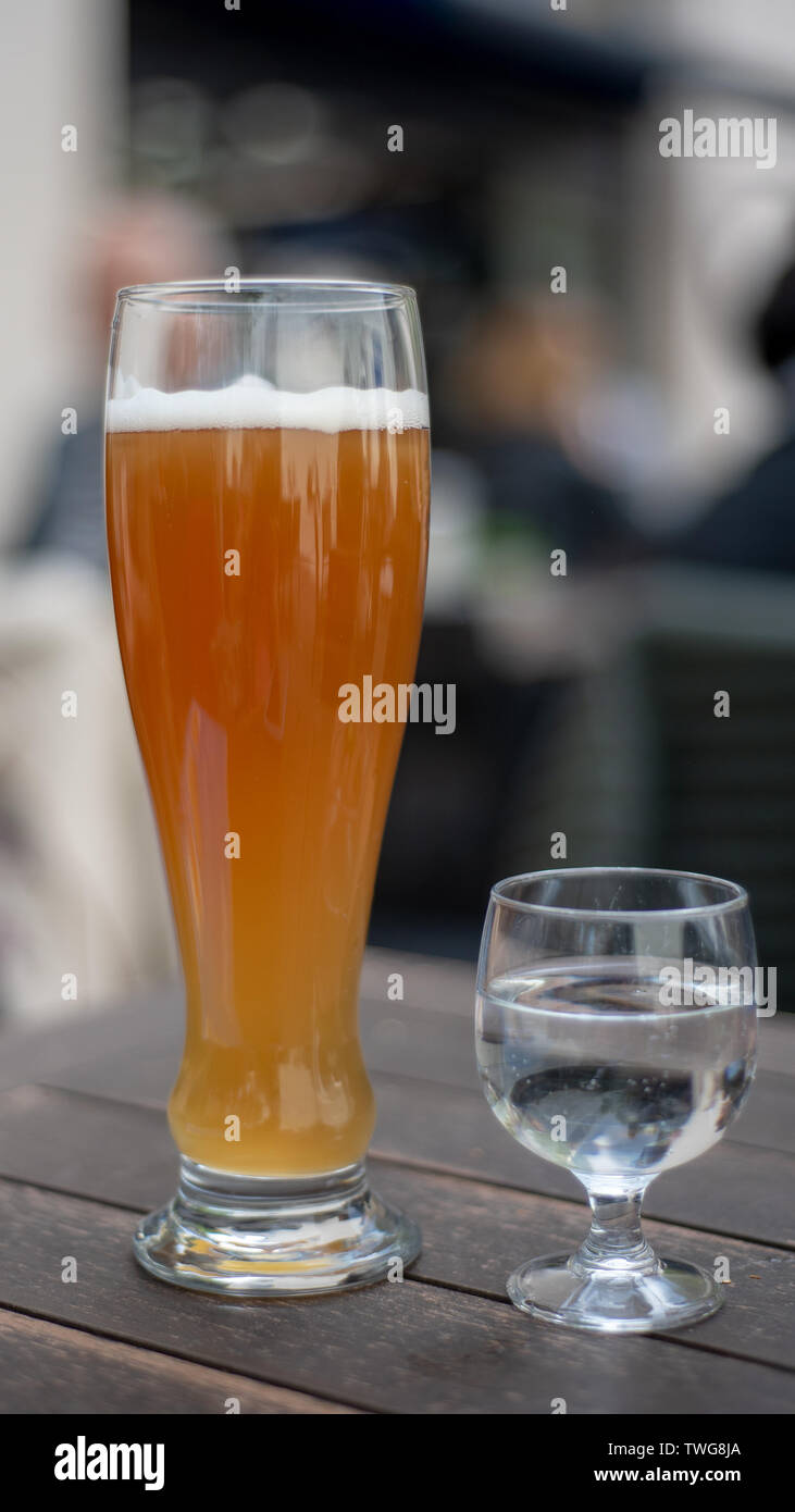 Weißbier auf dem Tisch voller Bier mit halb vollen Glas Mineralwasser auf hölzernen Tisch draußen serviert, von der Seite gesehen Stockfoto