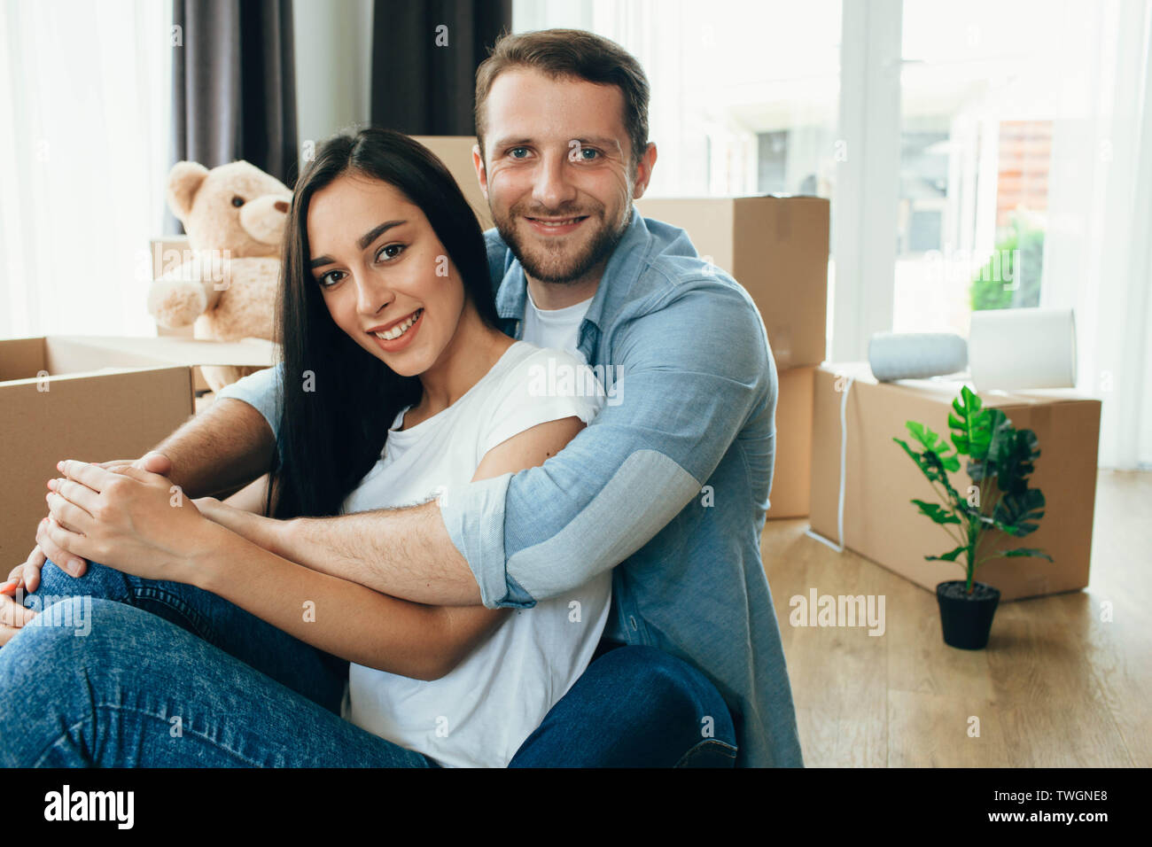 Glückliches Paar, neues Zuhause. Ihre sitzen auf dem Boden in Ihrem neuen Zuhause mit vielen Kartons auf Hintergrund Stockfoto