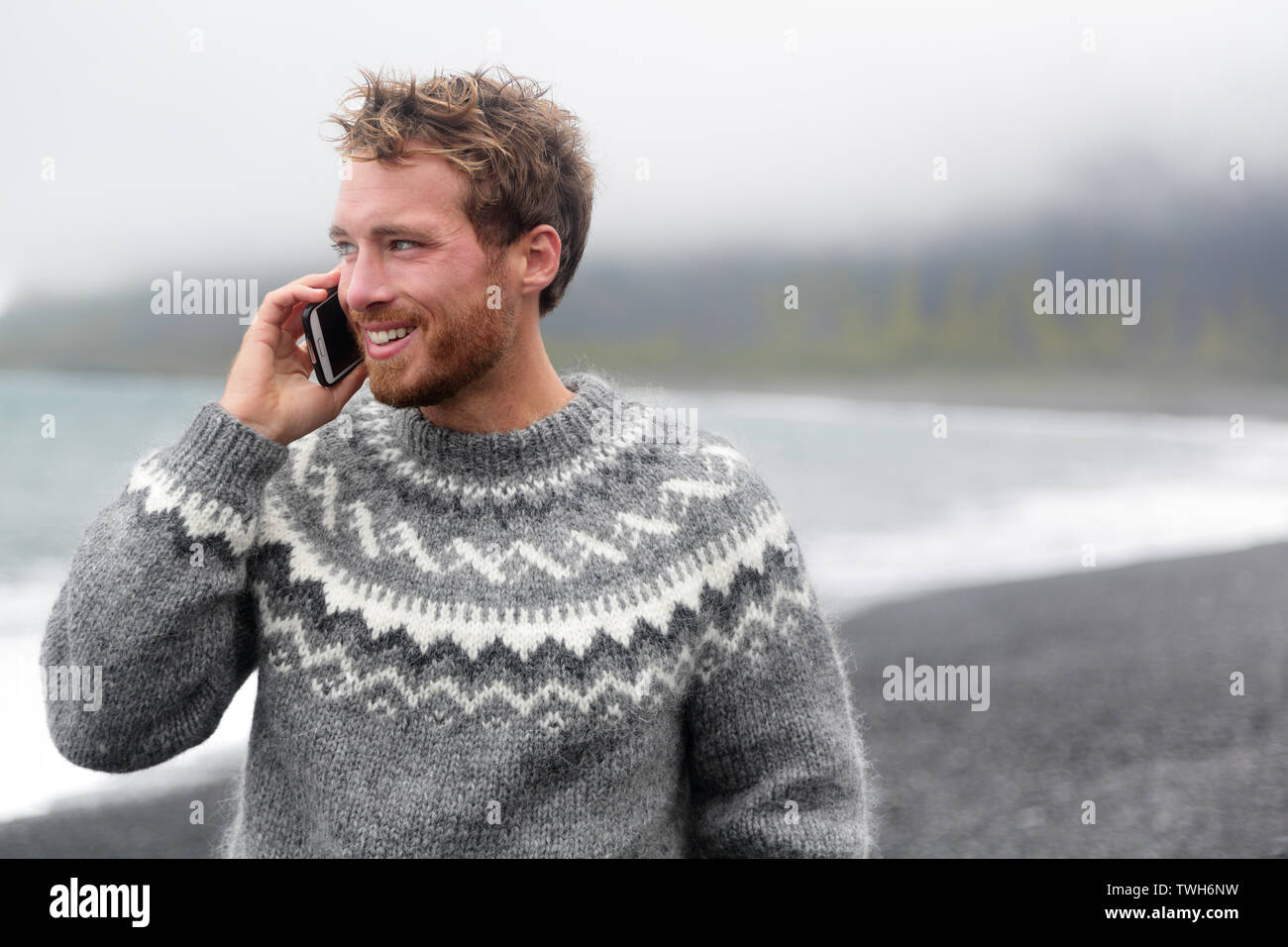 Smart phone Mann auf dem Smartphone zu Fuß auf schwarzem Sand Strand auf Island isländische Pullover tragen. Stockfoto