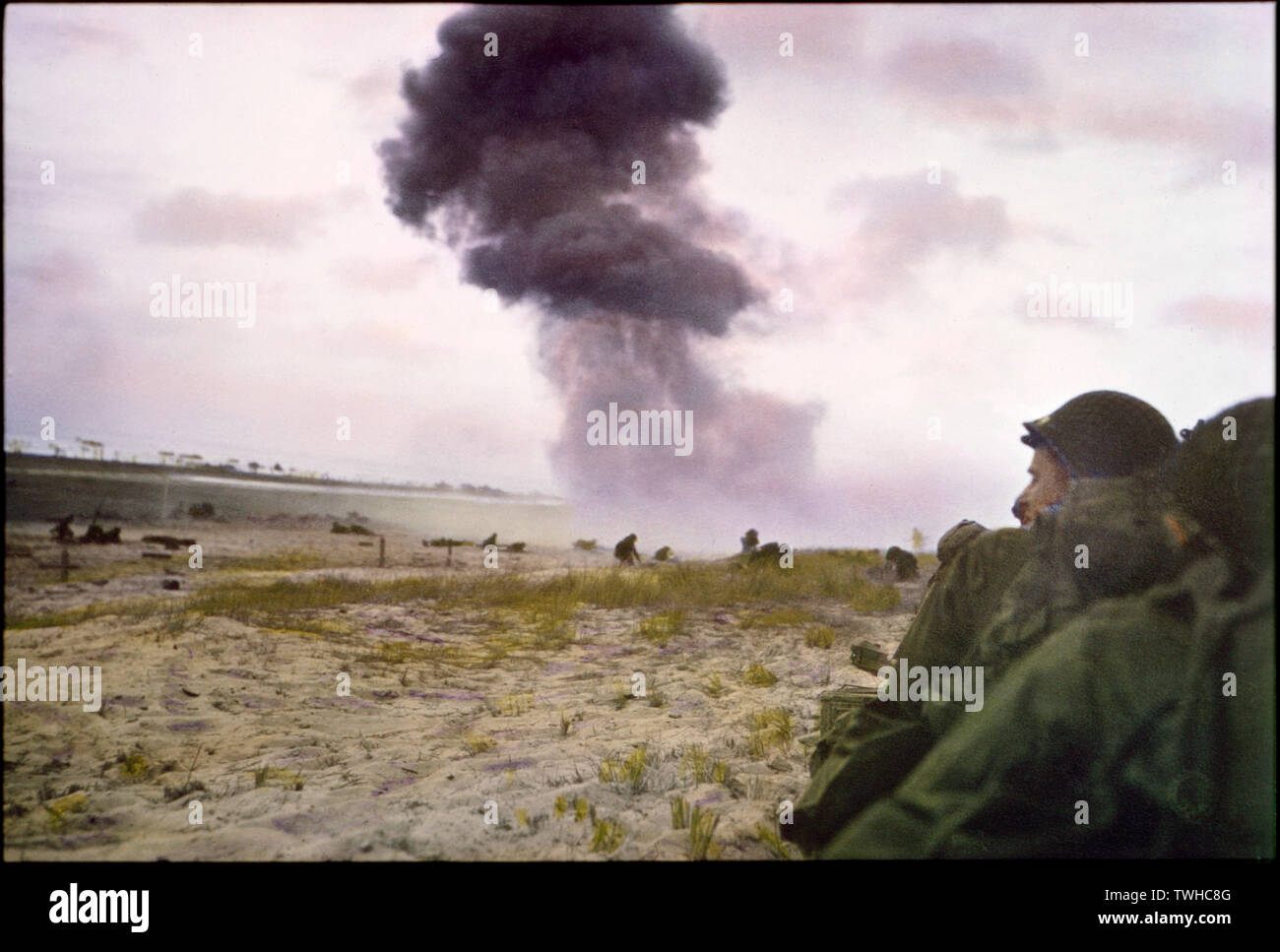 Us-Soldaten schützen sich vor feindlichen Feuer als 88-mm-Schale aus Deutschen Haubitze explodiert im Hintergrund, Utah Beach, Normandie, Frankreich, Juni 1944 Stockfoto