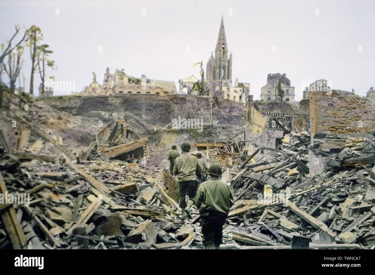 Amerikanische Infanterie Patrouille zu Fuß durch die Ruinen der französischen Stadt, Saint-Lo, nachdem es von den Deutschen, den Südturm der Kirche Notre Dame de Saint-Lo im Hintergrund, die Schlacht in der Normandie, Saint-Lo, Frankreich, Juli 1944 erfasst wurde Stockfoto