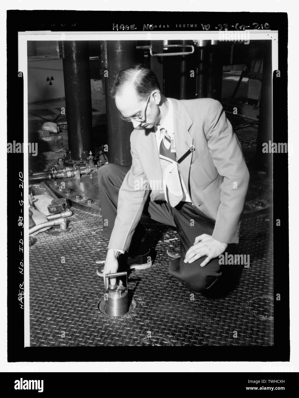 Wissenschaftler demonstriert, indem ein Kaninchen CATCHER IN EINES DER VERTIKALEN TEST LÖCHER AN DER OBERSEITE DER MTR an. Betätigungsstange ANTRIEBE SIND HINTER IHM NACH LINKS. INL NEGATIVE Nr. 56-513.; Jack L. Anderson, Fotograf, 2-13-821 - Idaho National Engineering Laboratory, Test Reactor, Materialien und Technik Test Reaktoren, Scoville, Butte County, ID Stockfoto