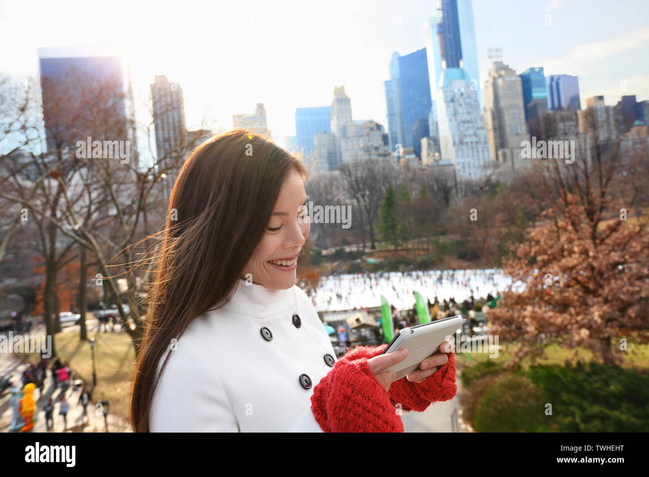 Frau auf Tablet-Smartphone im Central Park, New York City in den späten Herbst Winter mit Eisbahn im Hintergrund. Offenes Lächeln, multi-ethnischen Mädchen auf Manhattan, USA. Stockfoto