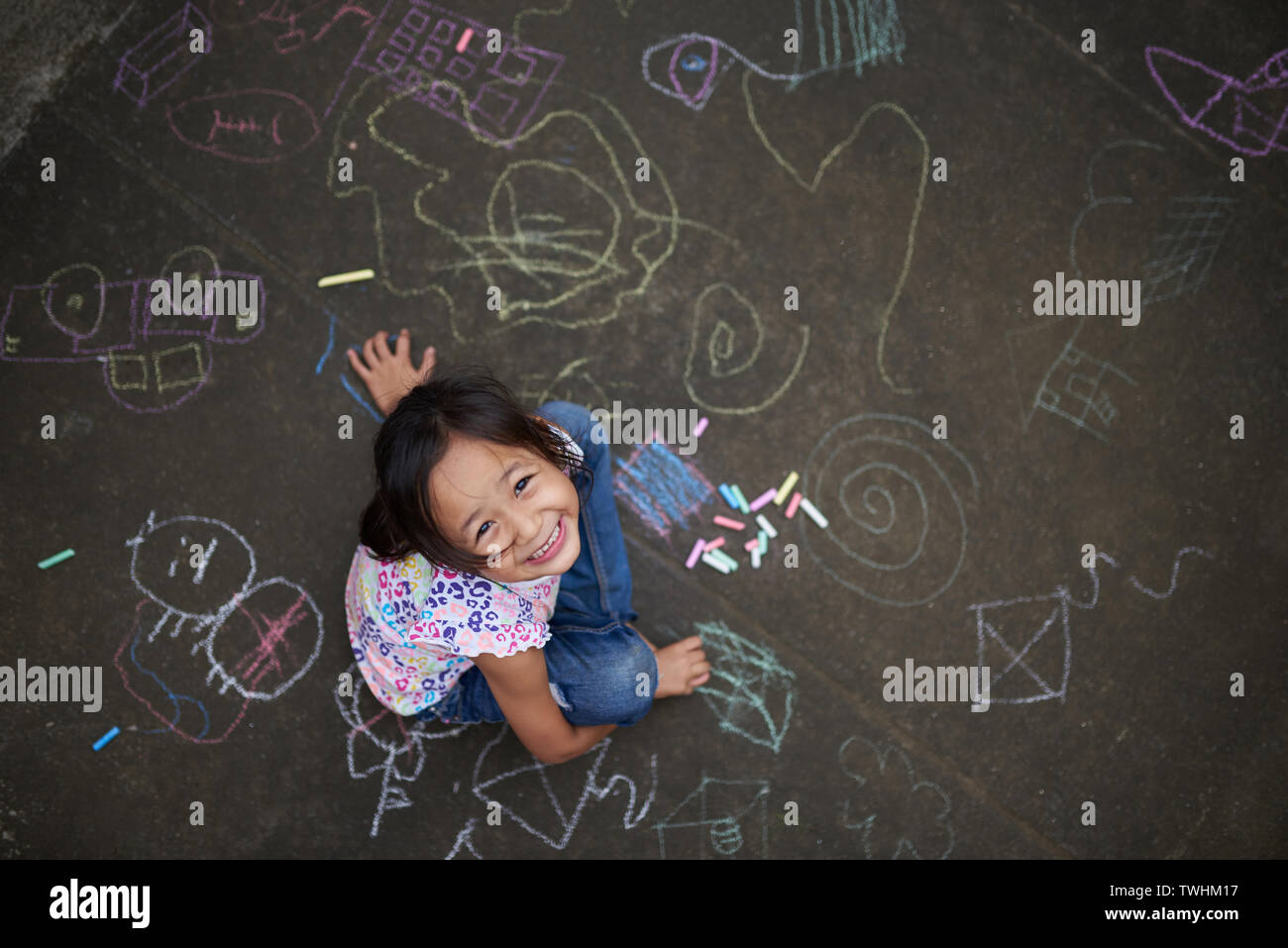 Asiatische Mädchen Zeichnen mit Kreide auf Asphalt. Kreidezeichnungen von einer Filipina Kid. Filipina Mädchen von 7 Jahren spielen mit Kreide. Stockfoto