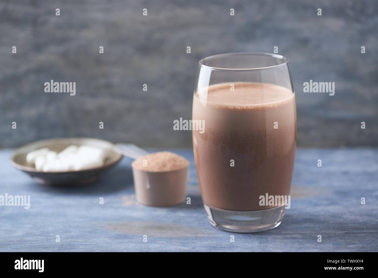 Glas Schokolade Protein Shake mit Milch und Banane. Whey Protein in Schaufel und BCAA Aminosäuren im Hintergrund. Stockfoto