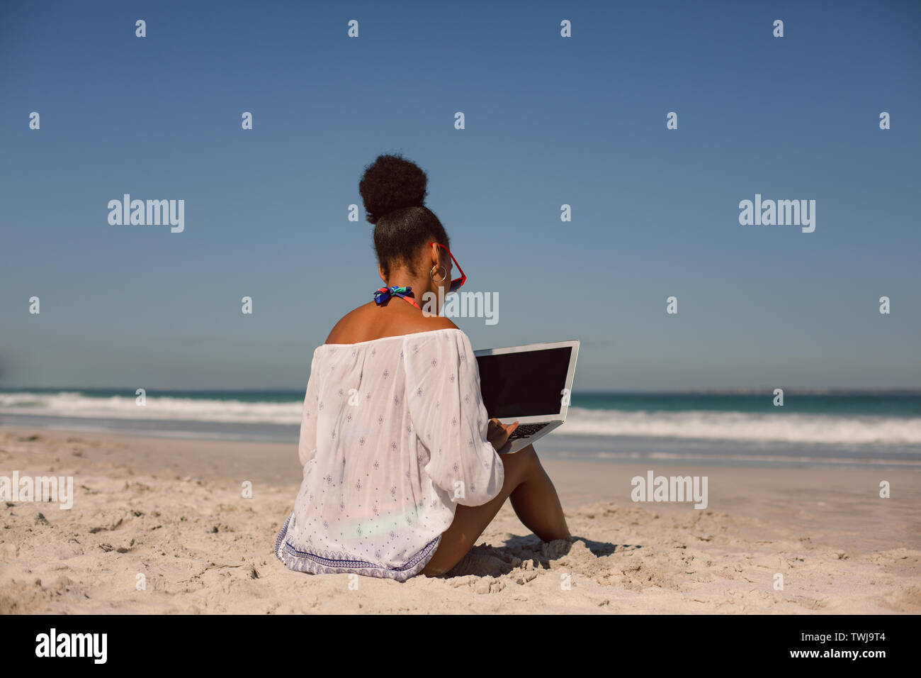 Frau sitzt auf Sand und mit Laptop am Strand in der Sonne Stockfoto