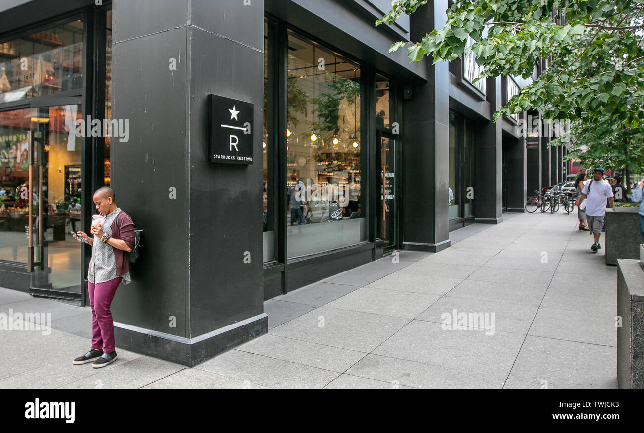 New York, 6/6/2019: Frau prüft Ihr Smartphone von einem Eingang zu einem Starbucks finden Outlet in Midtown Manhattan. Stockfoto