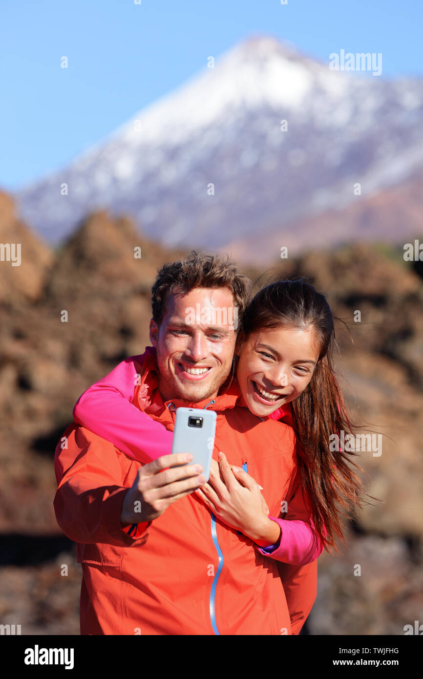 Selfie paar Wandern in schöner Natur mit Smartphone. Glückliches Paar zu Fuß genießen Ansehen und Aufnehmen von Bildern mit der Smart Phone. Mann und Frau, die von Vulkan Teide auf Teneriffa, Kanarische Inseln. Stockfoto
