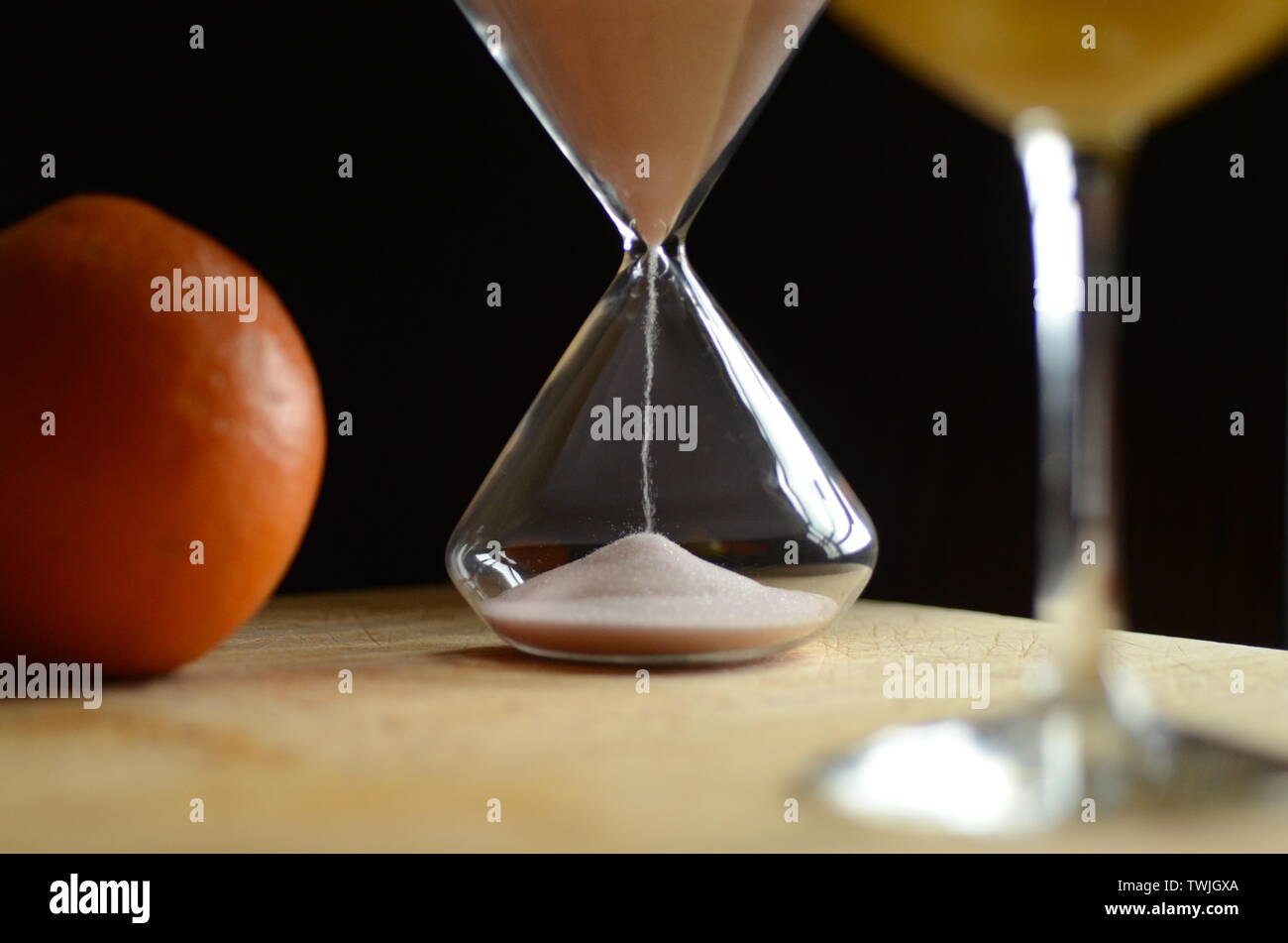 Frisches LEBEN: Eine Orange sitzt auf einem Schneidebrett neben hausgemachtem frischen Saft und einer Sanduhr. Stockfoto